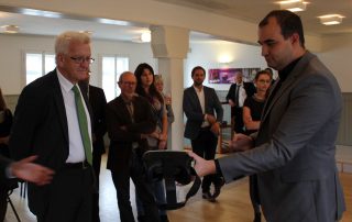 Ministerpräsident Kretschmann kriegt VR Headset vorgestellt von Geschäftsführer Florian Beutenmüller